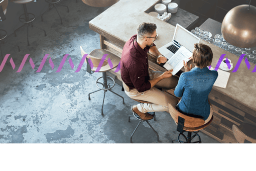 Image of two workers sitting on stools at a counter with a laptop, reviewing paperwork